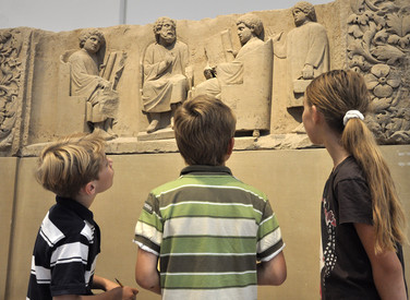 Kinder, die vor einem antiken Schulrelief stehen